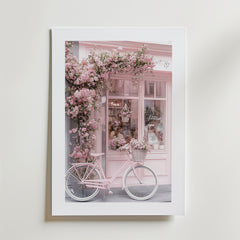 La Vie en Rose Poster by Bozetto föreställer en butikslokal i mjuka rosa toner, blommande blommor och en rosa vintage cykel, vilket skapar en romantisk pastell look med en elegant, lyxigt matt yta.