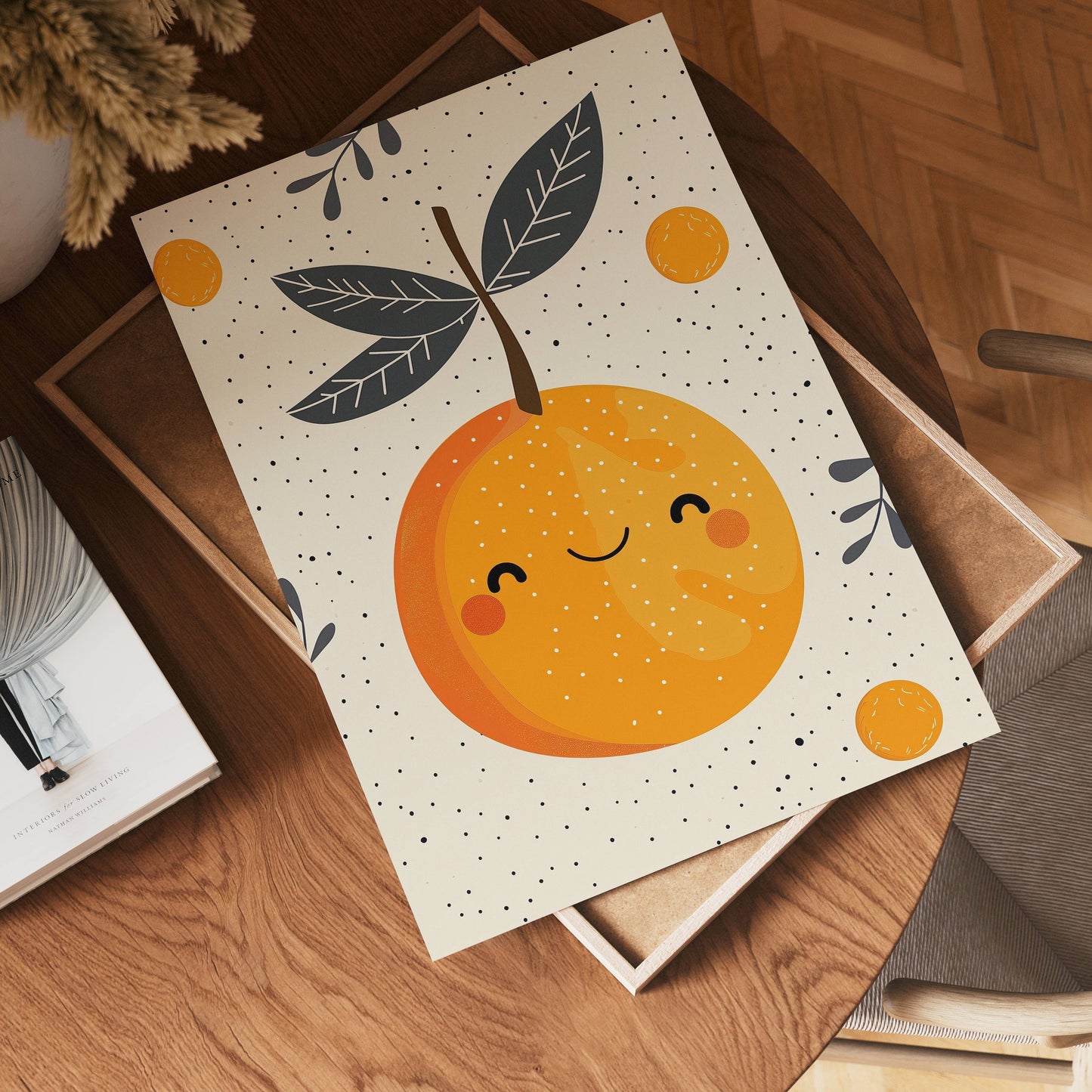 The no-9 art print features a cheerful orange with a smiling face and leaves, displayed on a wooden table among books and decor in a cozy, sunlit room.