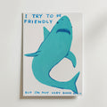 Bozetto Friendly Shark Poster visar en blå haj med ett sorgset ansikte och texten "I try to be friendly but I'm not very good at it" i blå bokstäver mot en vit bakgrund.