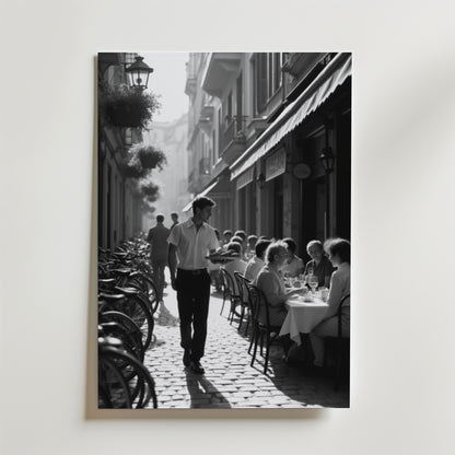 Charming Street Café Poster från Bozetto visar en svartvit scen av ett livligt utomhuscafé med gäster, en servitör och cyklar på en kullerstensgata - perfekt att visa på premiumpapper.