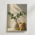 En spräcklig vas med bladgröna grenar står bredvid en brun papperspåse fylld med citroner och limefrukter. Solljuset kastar mjuka skuggor och framhäver den lyxigt matta ytan på Bozetto Ceramic Vase Lemon Love poster.