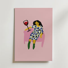 På postern Wine Down Poster från Bozetto syns en minimalistisk kvinna med mörkt hår i en mönstrad klänning och gröna boots, som slappnar av i en rosa stol med rödvin mot en rosa bakgrund. Tryckt på premiumpapper - perfekt för stilfulla inredningar.