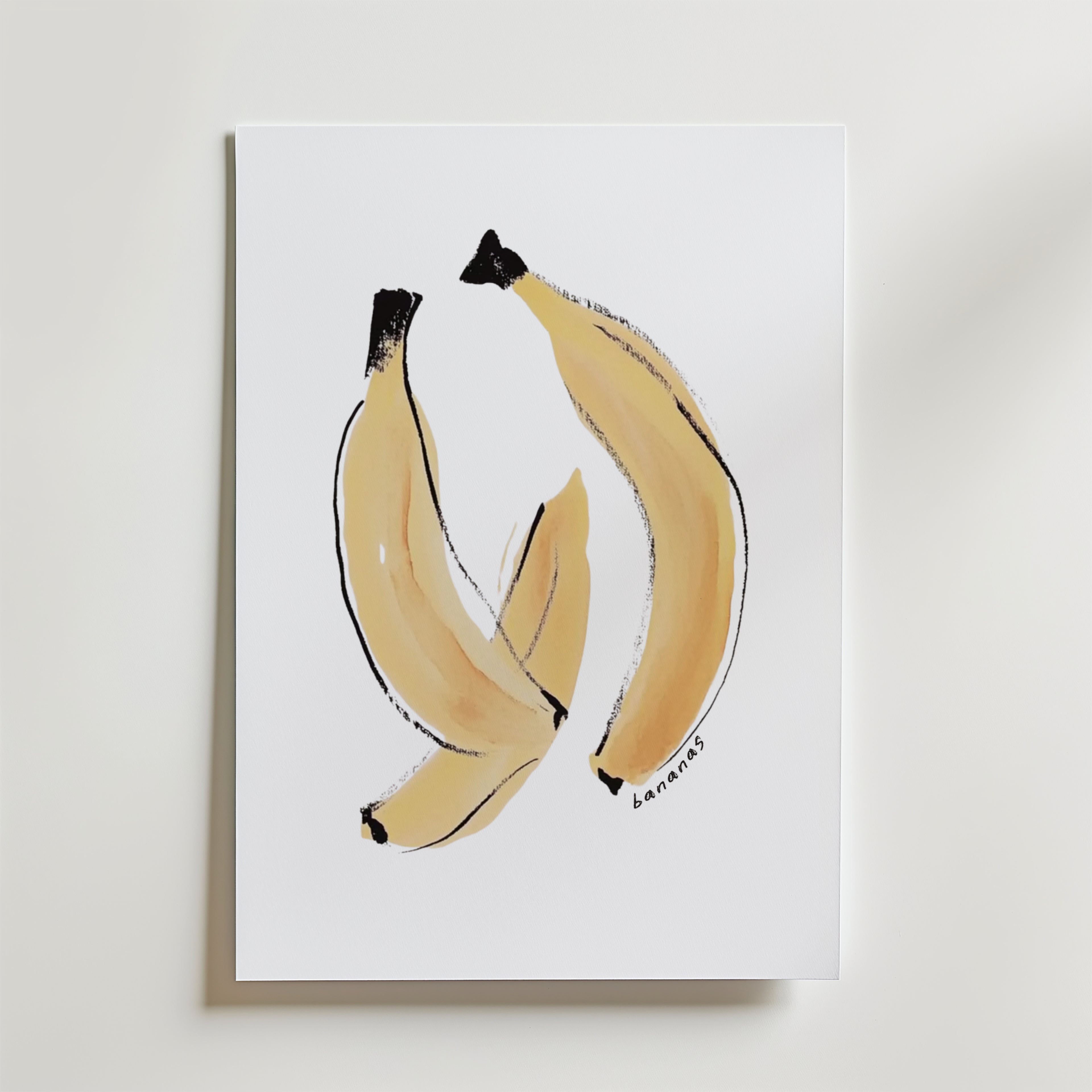 Bozetto Banana Joy Poster visar tre bananer på en vit bakgrund med minimalistiska penseldrag i ljusgult och svart. "Bananas" är handskrivet längst ner till höger, vilket skapar ett unikt konstverk på premiumpapper.