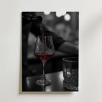 Bozetto Pouring Passion Wine Poster visar rött vin som hälls upp i ett glas på en mörk yta bredvid ett tomt glas, med mjukt suddiga bokeh-ljus som förstärker skönheten i vin i rörelse.