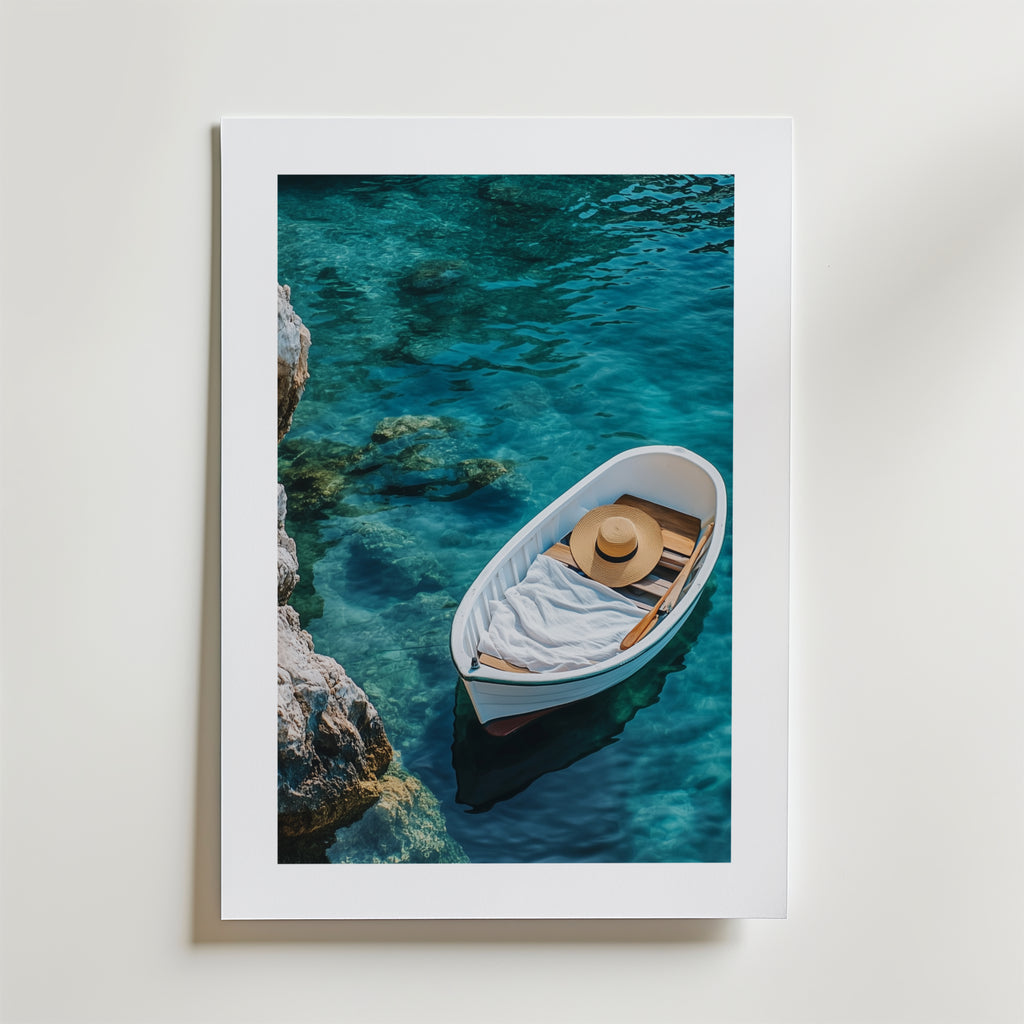 På postern Somewhere to Float Poster från Bozetto syns en liten vit roddbåt på klart turkost vatten nära klippor, med en vit filt och stråhatt som ger en lugn och somrig känsla. Tryckt på FSC-certifierat premiumpapper med högkvalitativ finish.