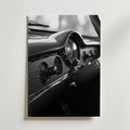 Bozetto's Old School Car Dashboard Poster visar ett svartvitt foto av en klassisk bils ratt, hastighetsmätare och vintagevred, tryckt på premiumpapper och uppsatt på en ljus vägg.