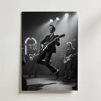 Bozetto Rock 'n' Roll Vibes Poster föreställer en svartvit scen med en gitarrist i kostym som hoppar i luften på scenen, tillsammans med andra musiker, scenljus och en jukebox, tryckt på premium matt finish papper.