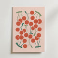 Cherry Rhythm Poster från Bozetto visar ett lekfullt, abstrakt kluster av röda körsbär med gröna stjälkar på en ljusrosa bakgrund, vilket ger en livlig, somrig känsla.