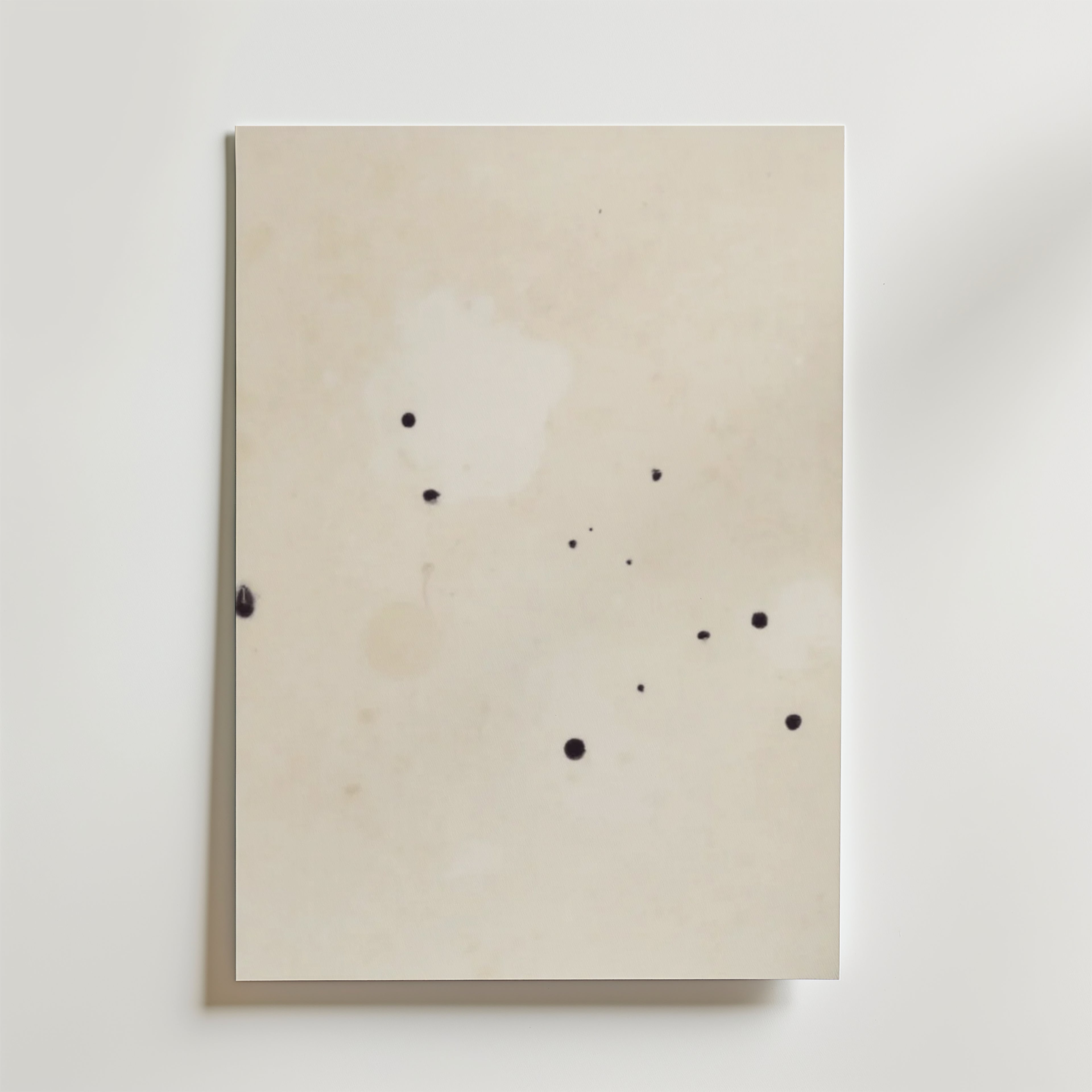 Postern Abstract Beige No.2 Poster by Bozetto har ett off-white premiumpapper med små, oregelbundna svarta bläckfläckar på den matta ytan, fotograferat mot en vit bakgrund.