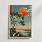 Bozetto Japanese Crane Poster föreställer tranor i en tall och vid en sjö i solnedgången, med en stark röd-orange sol, blå himmel och japansk kalligrafi uppe till vänster, allt i en slående träsnittsstil.