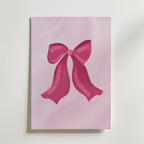 Bozetto Pink Ribbon Charm Poster har en glänsande rosa rosett på en mjuk ljusrosa bakgrund, perfekt som en romantisk poster eller snygg väggdekor mot en vit yta.