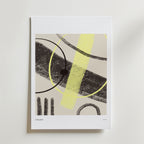 Bozetto Modern Tension Poster har djärva svarta linjer, ett gult penseldrag och överlappande cirklar på en ljusbeige bakgrund, placerad i en vit ram mot en slät vägg.