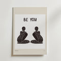 Be Your Poster från Bozetto föreställer två abstrakta, sittande svarta figurer som står vända mot varandra under en fet "BE YOU"-text som inspirerar till autenticitet på en vit bakgrund med en beige kant.
