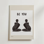 Be Your Poster från Bozetto föreställer två abstrakta, sittande svarta figurer som står vända mot varandra under en fet "BE YOU"-text som inspirerar till autenticitet på en vit bakgrund med en beige kant.