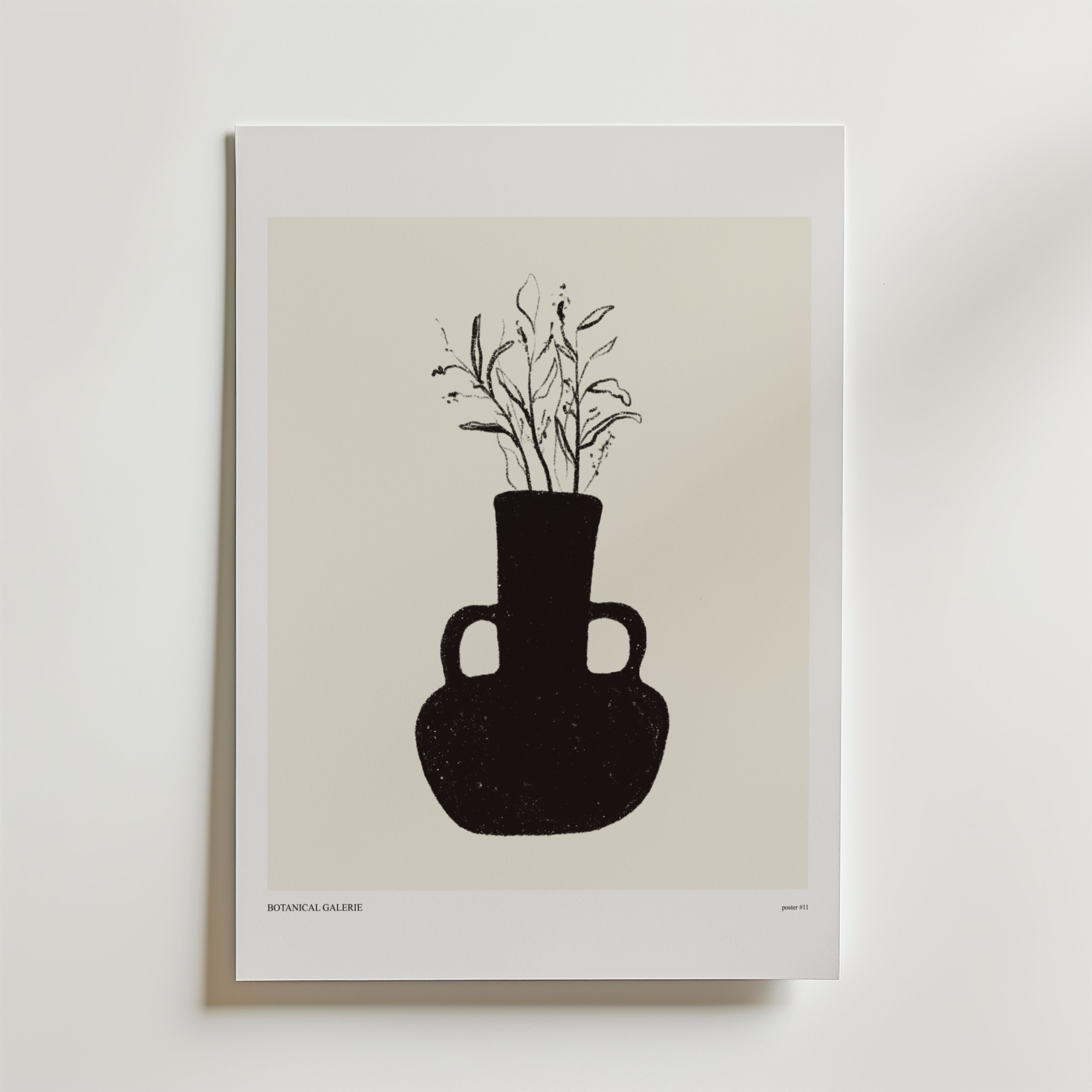 Rooted In Light Poster" från Bozetto föreställer en minimalistisk svart vas med två handtag och skira växtstjälkar på en beige bakgrund som ger jordnära inredning till en vit vägg.